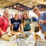 Photo of Junior Katelyn Pocock, sophomore Kyia Sparks, senior Hailey Arbuckle, and Everett Brothers, a visiting sophomore from Springville High School in Springville, Utah, got a little messy repackaging flour for Metro Caring’s food bank.