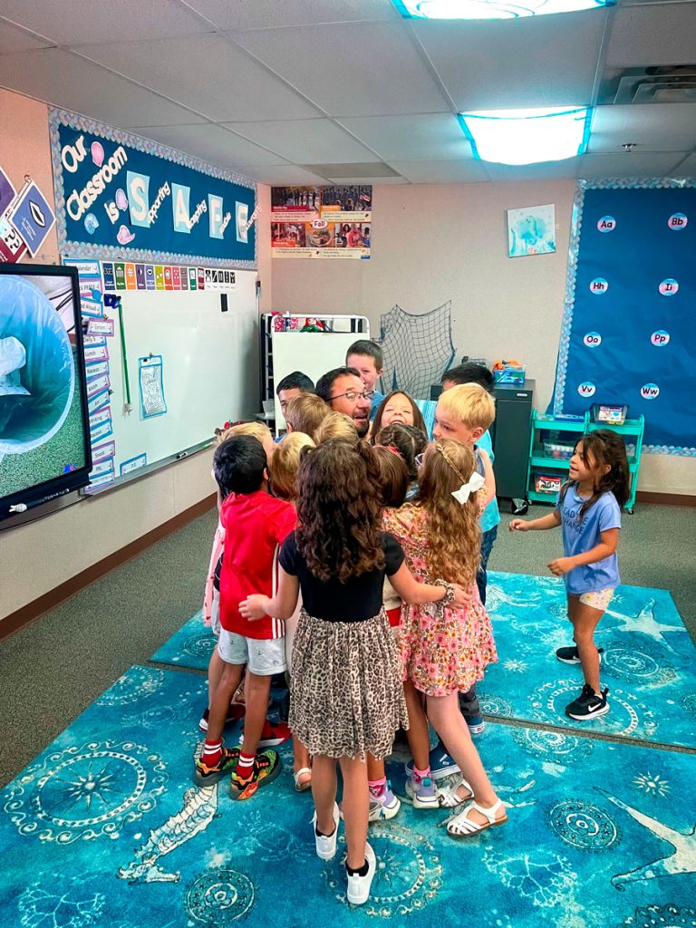 man getting hugged by his students in classroom